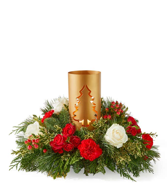 Holiday centerpiece arrangement featuring white roses, miniature red carnations, red hypericum berries, and seasonal greenery surrounding a gold metal candle holder with a cut-out tree design.