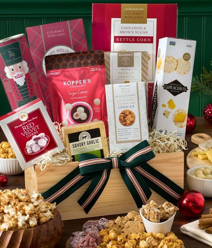  A holiday gift basket filled with assorted treats, including cinnamon and brown sugar kettle corn, peppermint wafer rolls, red velvet cookies, dipped peanuts, savory garlic cheddar cheese, Cubetti wafer cookies, gourmet popcorn, and Capeachio's crackers.