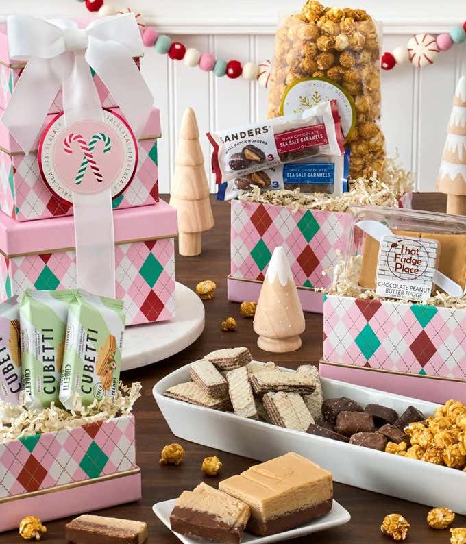 A festive pink and green argyle gift tower with a white bow, filled with chocolate peanut butter fudge, Cubetti wafer cookies, dark chocolate sea salt caramels, and caramel popcorn. A delightful holiday treat assortment perfect for gifting.