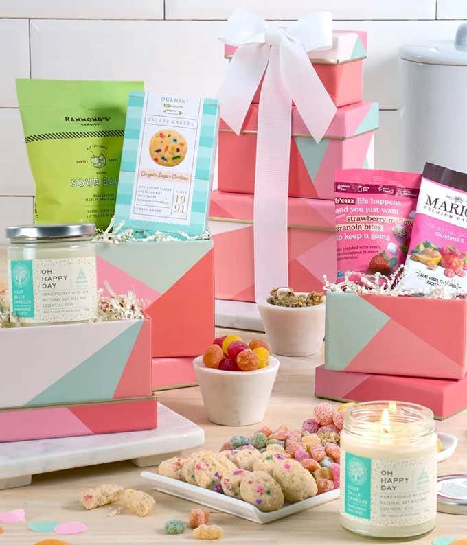Gift tower adorned with bow, featuring celestial sour gummies, natural sour candies, confetti sugar cookies, and strawberry-mallow granola bites, with 'Oh Happy Day' candle.