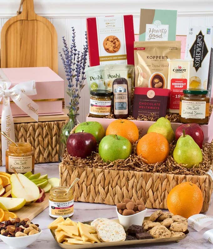 Gift basket with fresh apples, pears, and oranges, paired with gourmet snacks including crackers, cheeses, olives, caramel sauce, honey mustard, cookies, chocolates, and nut mix, arranged in woven baskets with sympathy ribbon accents.