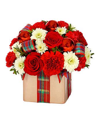 Red roses and red carnations in a square vase with a holiday ribbon