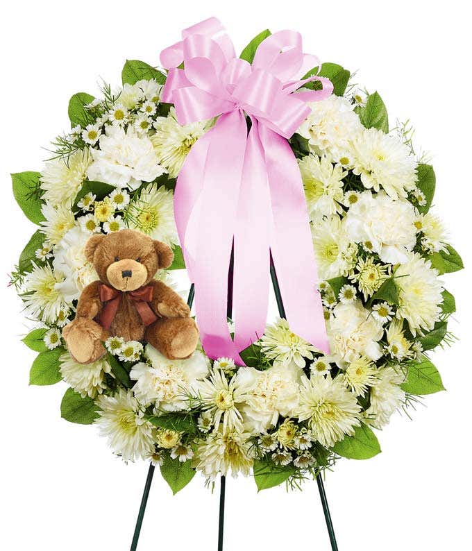 White floral funeral wreath with a pink bow and a teddy bear