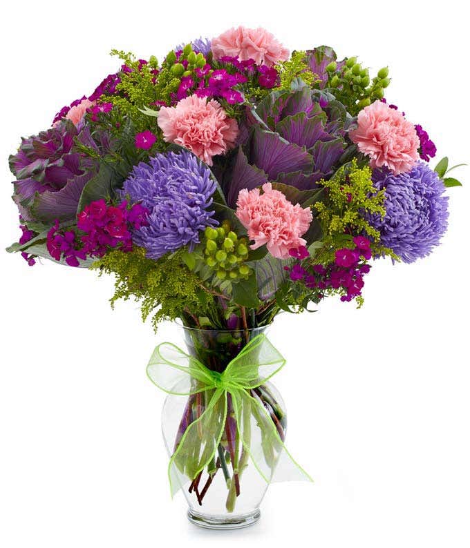 Pink carnations, purple kale and asters in glass vase with bow