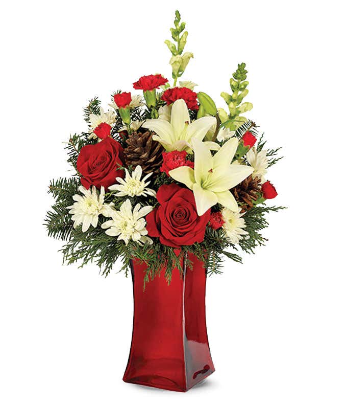 Red roses are arranged by a florist with white lilies, red carnations and pinecones in a tall red vase