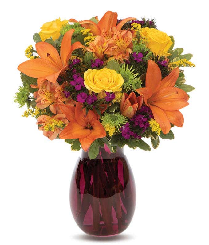 Orange lilies, yellow roses and purple flowers in a fall-colored vase