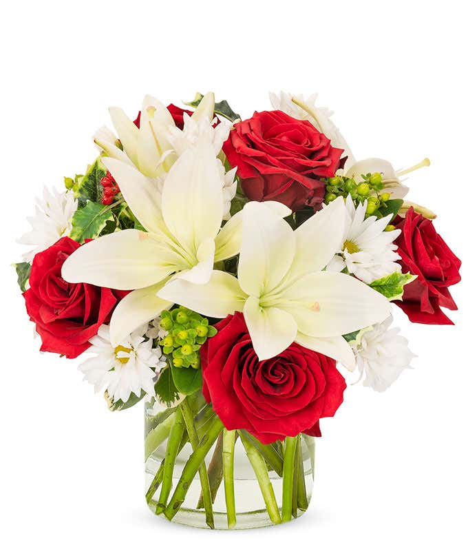 White lilies, red roses, and daisies arranged into a short cylinder vase.