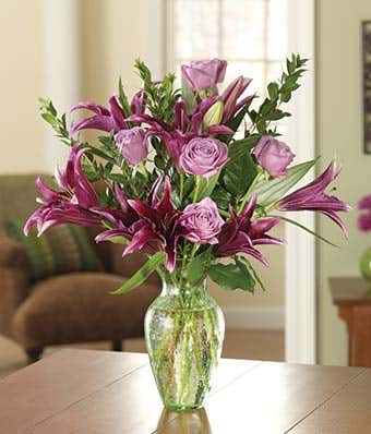 Purple roses and dark purple lilies in a glass vase