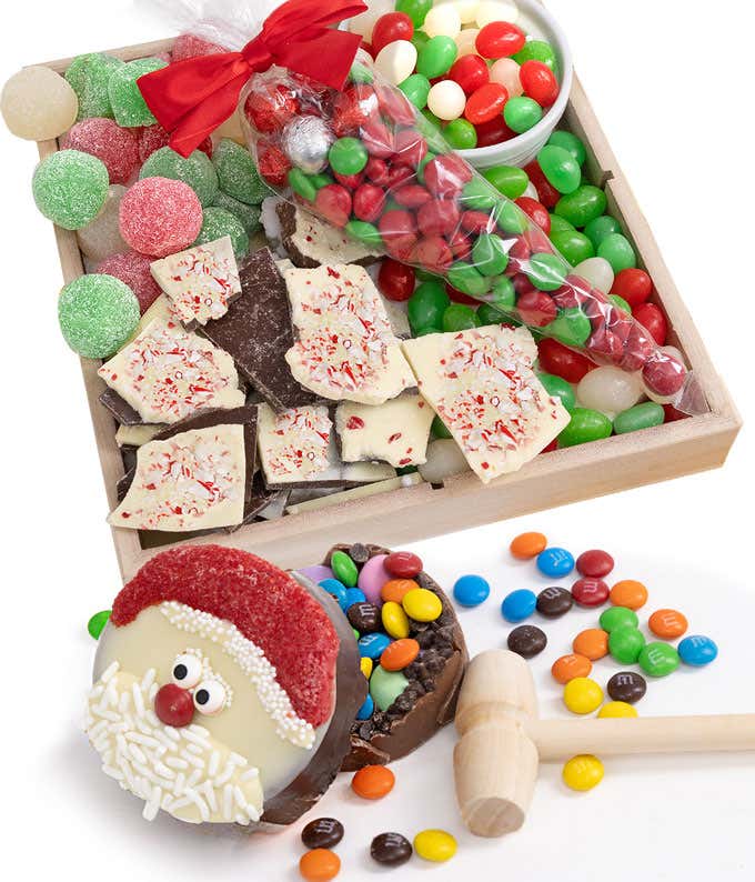 Chocolate candies, gum drops, jelly beans, peppermint bark with milk and white chocolate, a chocolate breakable with a Santa character design next to a wooden mallet in a wooden gift box
