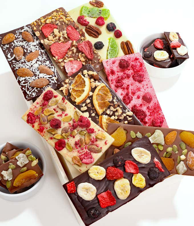 Eight bars of chocolate bark, varying in white, dark, and milk chocolate with dried fruits and nuts on top of each bar in a wooded gift box