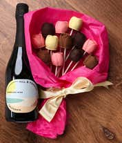 A bouquet of Belgian chocolate roses in milk, dark, and white chocolate, wrapped in pink tissue paper and tied with a cream ribbon, accompanied by a bottle of Hill & Harbor Sparkling Wine