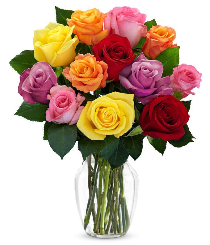  A bouquet of multicolored roses in a clear vase, featuring red, pink, orange, yellow, peach, and lavender blooms, arranged with green leaves for a vibrant and cheerful display.