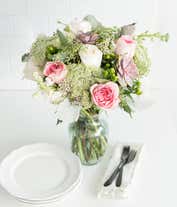 Alternative image 3 for A floral arrangement featuring white roses, pink roses, succulents, white stock, hypericum berries, Queen Anne's lace, white waxflower, and seeded eucalyptus, with an optional glass vase.