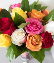 Alternative image 3 for A bouquet of multicolored roses in a clear vase, featuring red, pink, orange, yellow, peach, and lavender blooms, arranged with green leaves for a vibrant and cheerful display.