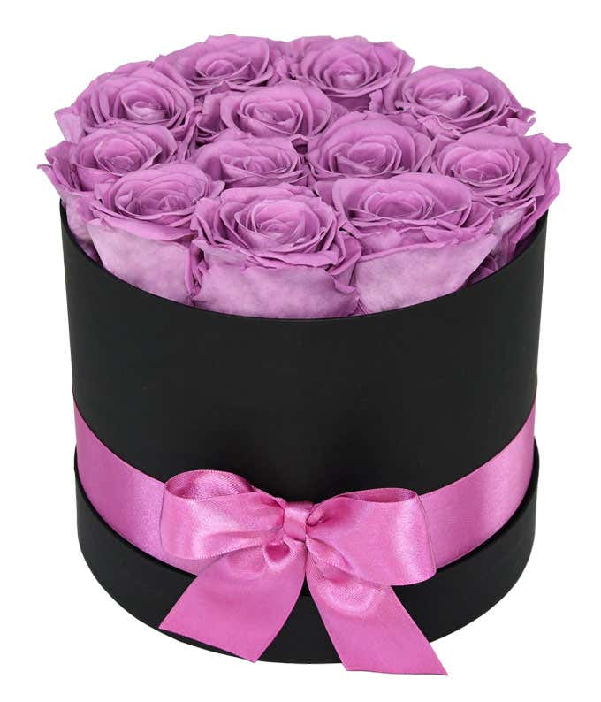 One dozen light purple preserved roses arranged into a black hat box with a purple ribbon.
