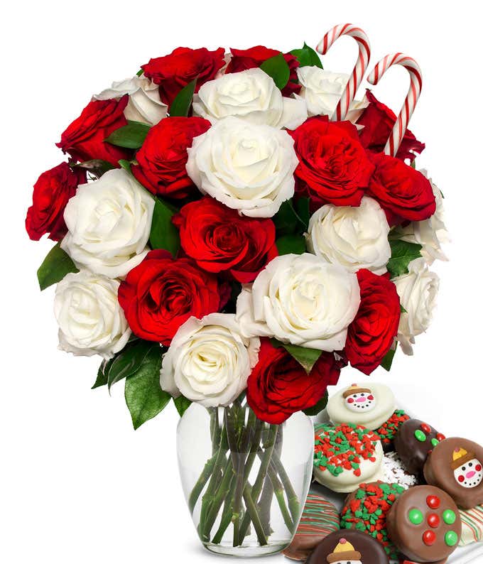 12 red and 12 white roses and 2 candy canes popping out of a glass vase with some leaves showing. Next to it is a plate of chocolate cookies with red/green sprinkles, candy, and snowmen.