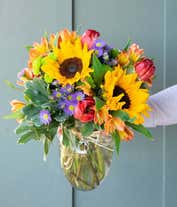 Alternative image 3 for A vibrant arrangement featuring sunflowers, pink tulips, red alstroemeria, purple Monte Casino asters, and green poms, optionally arranged in a glass vase. This lively mix offers a bright and cheerful display.
