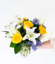 Alternative image 2 for An elegant floral arrangement featuring white Asiatic lilies, yellow roses, blue delphinium, and purple Monte Casino, optionally arranged in a glass vase. This vibrant mix offers a stunning and colorful display.