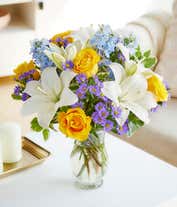Alternative image 4 for An elegant floral arrangement featuring white Asiatic lilies, yellow roses, blue delphinium, and purple Monte Casino, optionally arranged in a glass vase. This vibrant mix offers a stunning and colorful display.