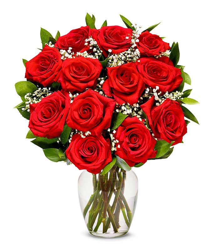 a bouquet of 12 red roses with small white flowers and greenery in between in a clear glass vase