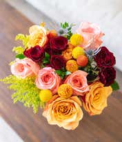 Alternative image 1 for  A vibrant floral arrangement featuring coral roses, peach roses, coral mini roses, yellow solidago, yellow craspedia, orange craspedia, and blue eryngium, complemented by a personal card message and optionally presented in a vase.