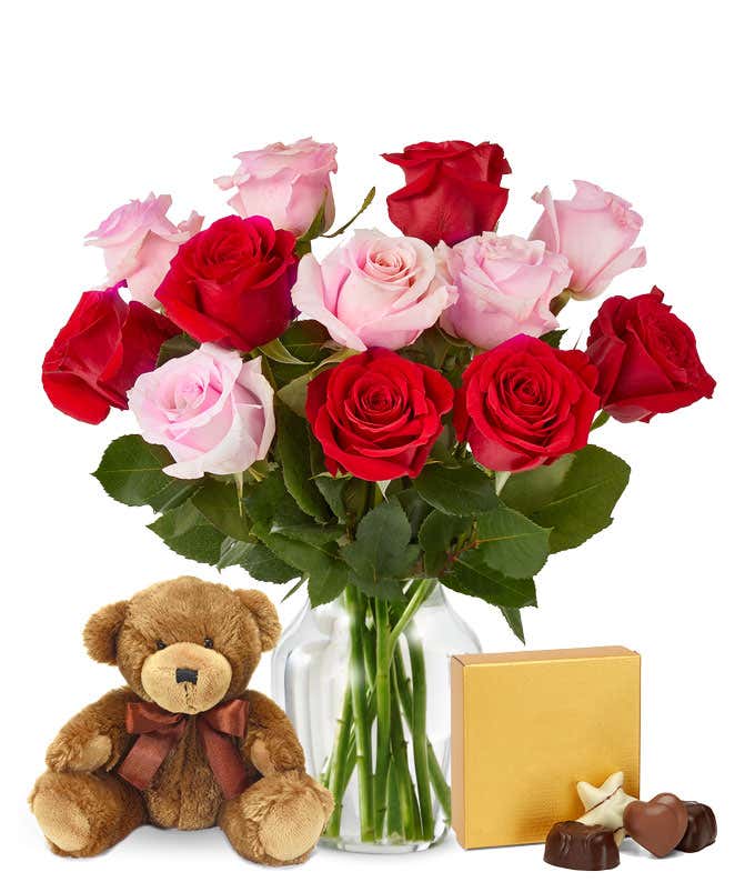 A bouquet of red and pink roses with lush greenery arranged in a clear glass vase.