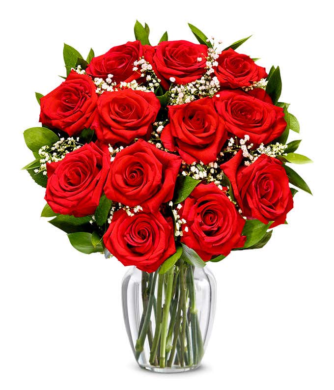 A bouquet of yellow roses, buttons, and sunflowers, blue hydrangea and delphinium, white mums, stock, and queen anne's lace and purple statice in a clear glass vase with a box of chocolates