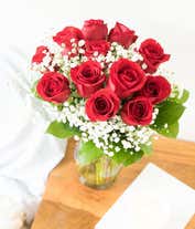 Alternative image 2 for a bouquet of 12 red roses with small white flowers and greenery in between in a clear glass vase