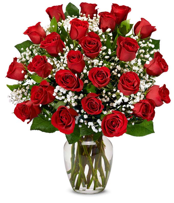 a bouquet of 24 red roses with small white flowers and greenery in between in a clear glass vase