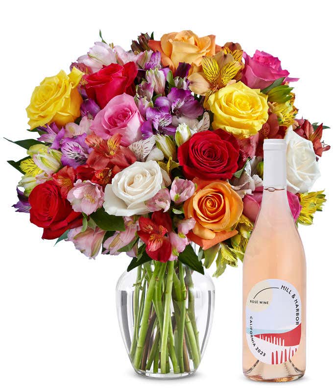 A mix bouquet of roses and alstroemeria fills a clear glass vase and is paired with a bottle of Hill & Harbor California Pinot Noir.