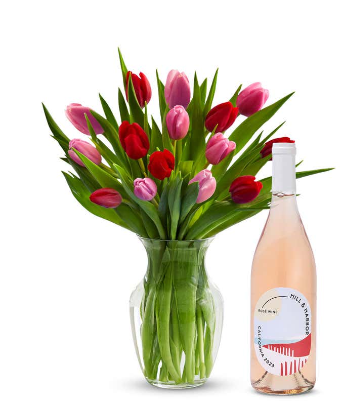 A clear glass vase filled with 15 stems of mixed red and pink tulips and bright green stems sits beside a bottle of Hill & Harbor California Rosé.