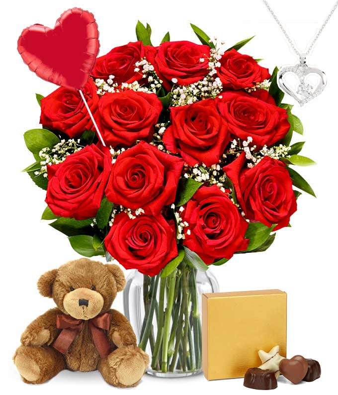 One Dozen Red Roses in clear glass vase with a red heart mylar balloon, silver heart necklace, a box of chocolates, and teddy bear