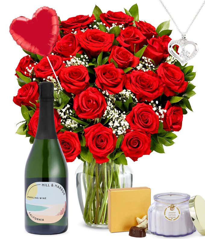 Two Dozen Red Roses in a clear glass vase with a box of chocolates, a silver heart necklace, red heart mylar balloon, a bottle of sparkling wine, and a dahlia & orchid scented candle