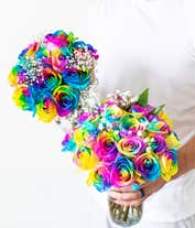 Alternative image 4 for A colorful bouquet of rainbow roses in a clear glass vase, with petals in vibrant hues of blue, yellow, pink, and purple, accented by baby's breath and green leaves, creating a bright and cheerful display.
