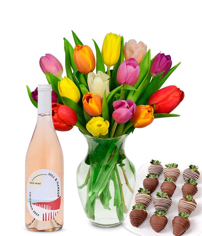 A clear glass vase filled with a 15-stem assortment of multi-colored tulips paired with a bottle of rosé wine and 12 chocolate-covered strawberries.