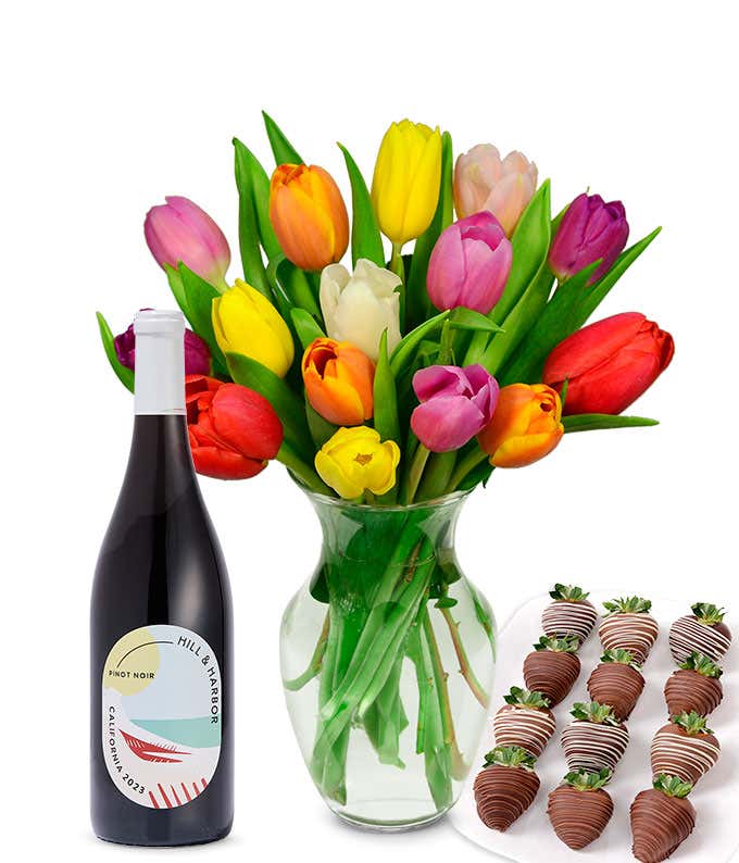 A clear glass vase filled with a 15-stem assortment of multi-colored tulips paired with a bottle of red wine and 12 chocolate-covered strawberries.