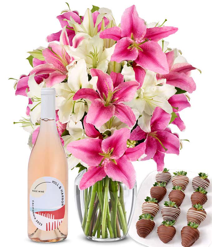 A bouquet of pink and white lilies arranged in a clear glass vase is paired with a bottle of Hill & Harbor Rosé and 12 chocolate-covered strawberries.