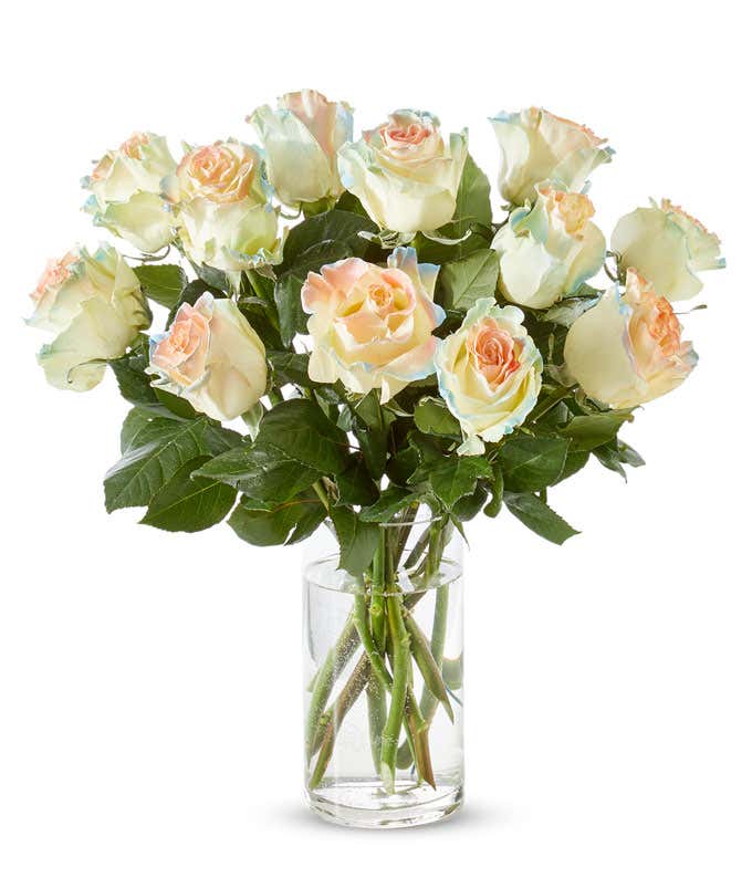 A bouquet in a rounded clear glass vase of 12 roses with greens, the background is dark and the roses are glowing bright blue.