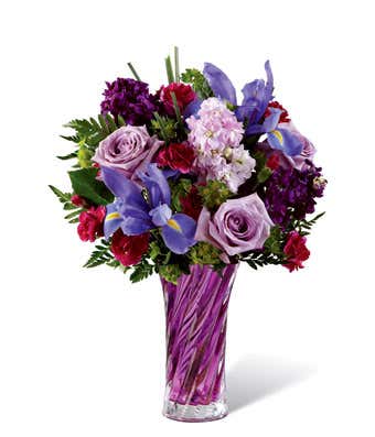 Purple roses are arranged with purple daisies, iris and gilly flowers in a purple vase