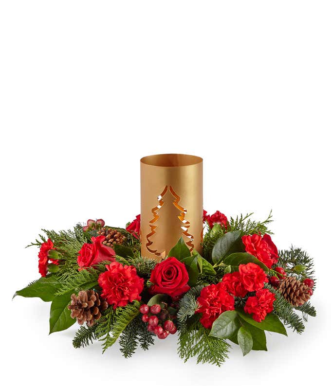 Centerpiece of red florals accompanied by seasonal greens, with a gold lantern in the center