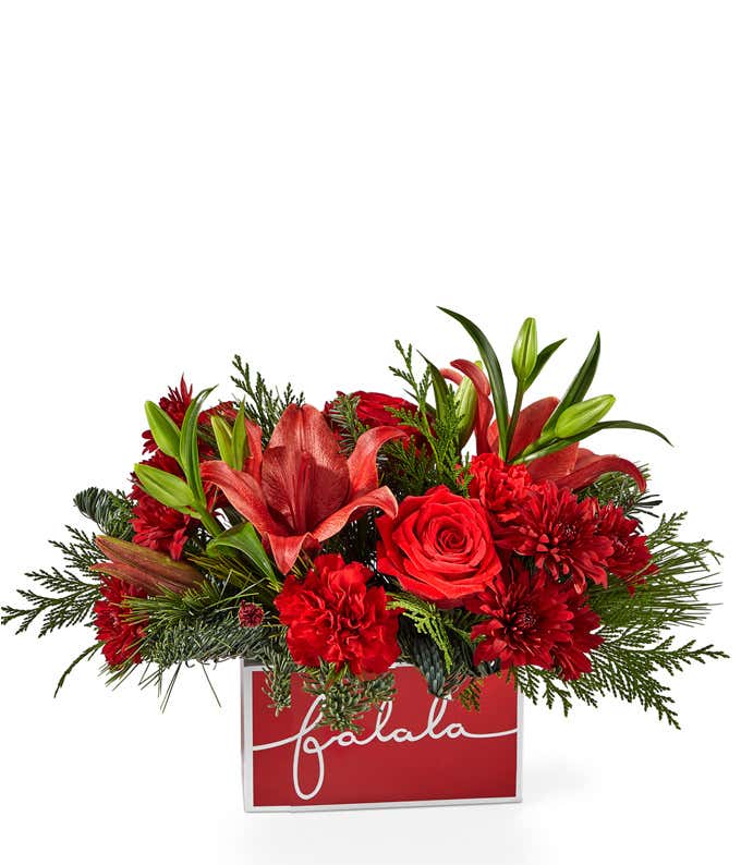 Red roses, carnations, and lilies mixed with assorted Christmas greens, and arranged into a red wooden container with the cursive test fa la la.