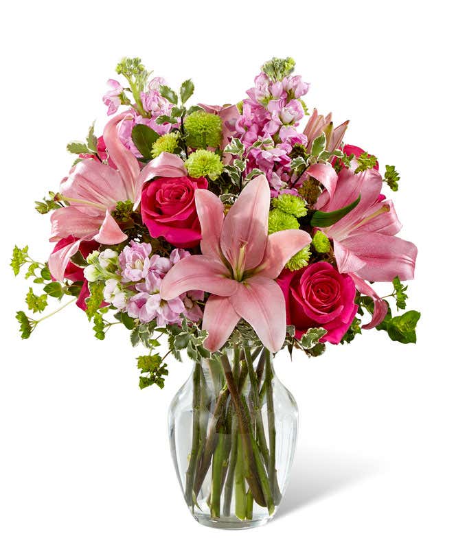 Pink lilies, roses, and gilly flowers, with fresh floral greens in a clear glass vase
