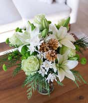Alternative image 2 for A festive arrangement with white Asiatic lilies, green roses, green and white poms, evergreens, displayed in a glass cylinder vase.