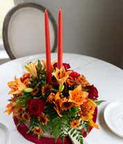 Alternative image 3 for A stunning floral centerpiece featuring red roses, red carnations, orange lilies, peach berries, and bronze cushion poms, complemented by two orange taper candles.