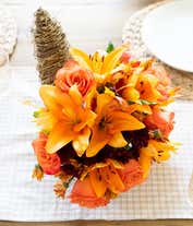 Alternative image 1 for A festive floral arrangement featuring orange lilies, orange roses, orange alstroemeria, and bronze daisies and poms, all beautifully displayed in a cornucopia basket.