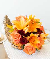 Alternative image 2 for A festive floral arrangement featuring orange lilies, orange roses, orange alstroemeria, and bronze daisies and poms, all beautifully displayed in a cornucopia basket.