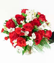 Alternative image 2 for A festive arrangement with red roses, red carnations, red mini carnations, white alstroemeria, and evergreens, beautifully displayed in a glass vase.