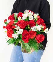 Alternative image 3 for A festive arrangement with red roses, red carnations, red mini carnations, white alstroemeria, and evergreens, beautifully displayed in a glass vase.