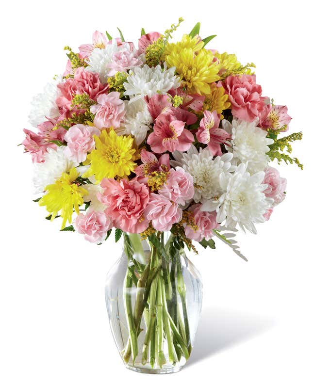 Full and round arrangement of pink roses, carns, and alstroemeria, mixed with white and yellow poms in a clear glass vase