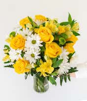Alternative image 1 for A bright floral arrangement featuring yellow roses, white daisies, yellow alstroemeria, and green poms, elegantly arranged in a glass vase. This sunny mix offers a cheerful and uplifting display.